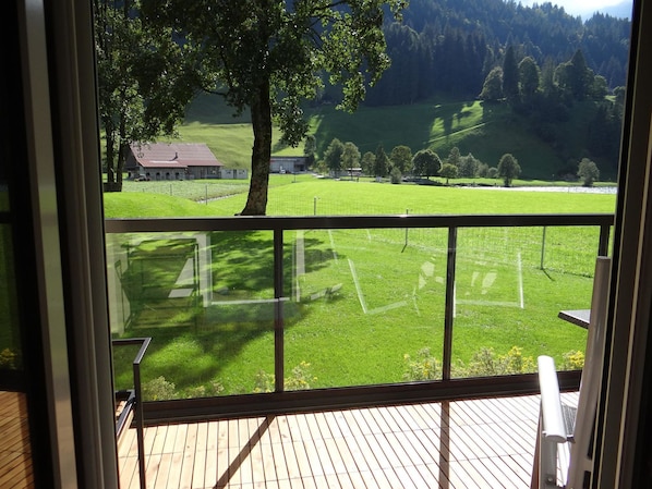 A balcony with a view of a green field and a building in the distance.