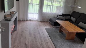 A modern living room with a flat-screen TV, a sofa, a wooden coffee table, and a fireplace.