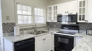 A kitchen with white cabinets, a microwave, stove, dishwasher, and a window with blinds.