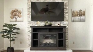 A living room with a stone fireplace, a mounted flat-screen TV, and two framed artworks on the walls.