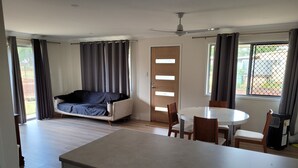 Ein modernes Wohnzimmer mit einer Couch, einem Esstisch mit Stühlen, einer Küchenzeile mit Arbeitsplatte und Schränken sowie einer Glastür, die auf einen Balkon führt.