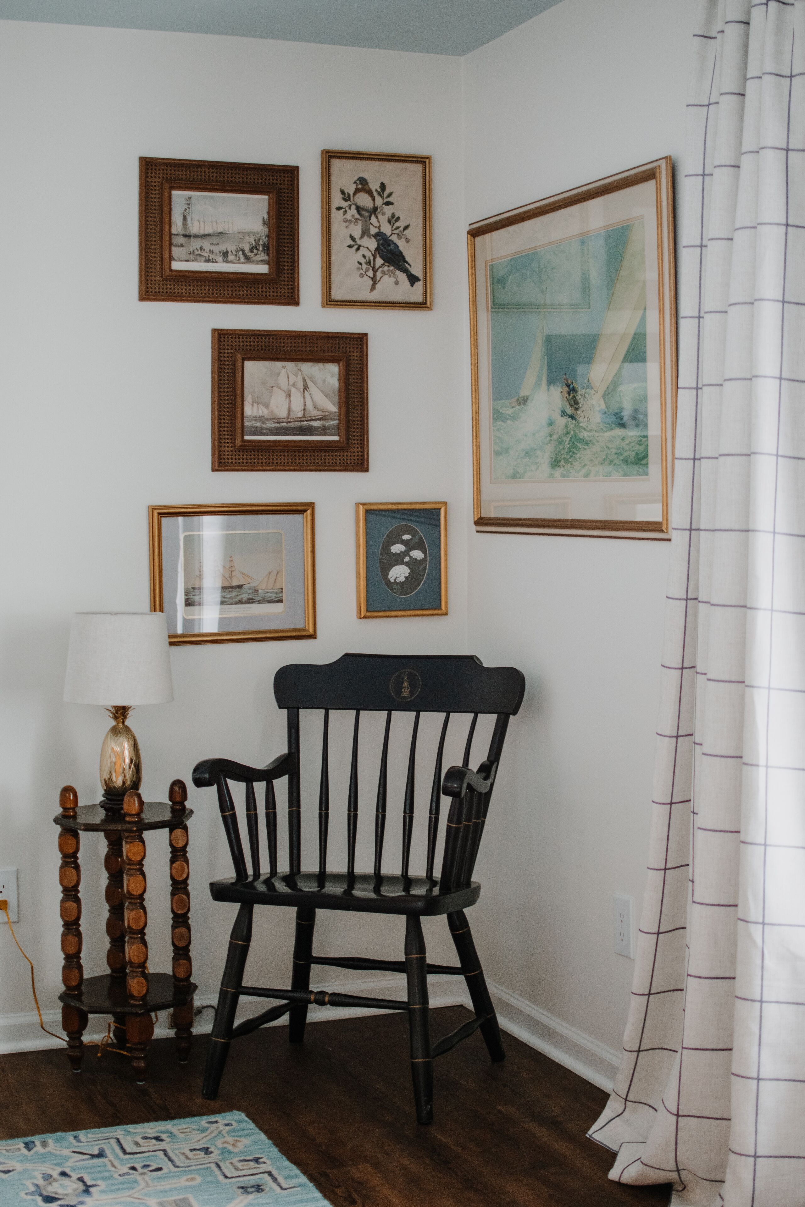 A room with a wooden floor, a black chair, a lamp, and framed pictures on the wall.