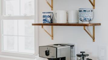 Une cuisine avec des étagères en bois où sont rangés divers ustensiles de cuisine, une machine à café et un récipient à sucre.