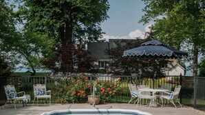 A swimming pool with a tiled edge, surrounded by a patio area with white metal chairs and a table. - Waterfront Rappahannock River Cottage, Private Pool, Kayaks, Fire Pit & Garden (Locust Hill)