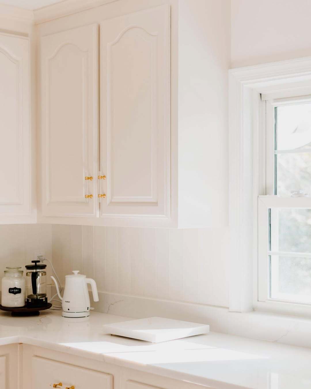 A kitchen with white cabinets, a window, and a coffee maker on the counter.