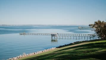 Een kalm meer met een houten steiger die het water in reikt, omgeven door grasachtige oevers en een rotsachtige kustlijn.