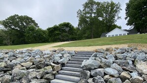 A stone staircase leading to a grassy area with a white building in the background. - Waterfront Rappahannock River Cottage, Private Pool, Kayaks, Fire Pit & Garden (Locust Hill)