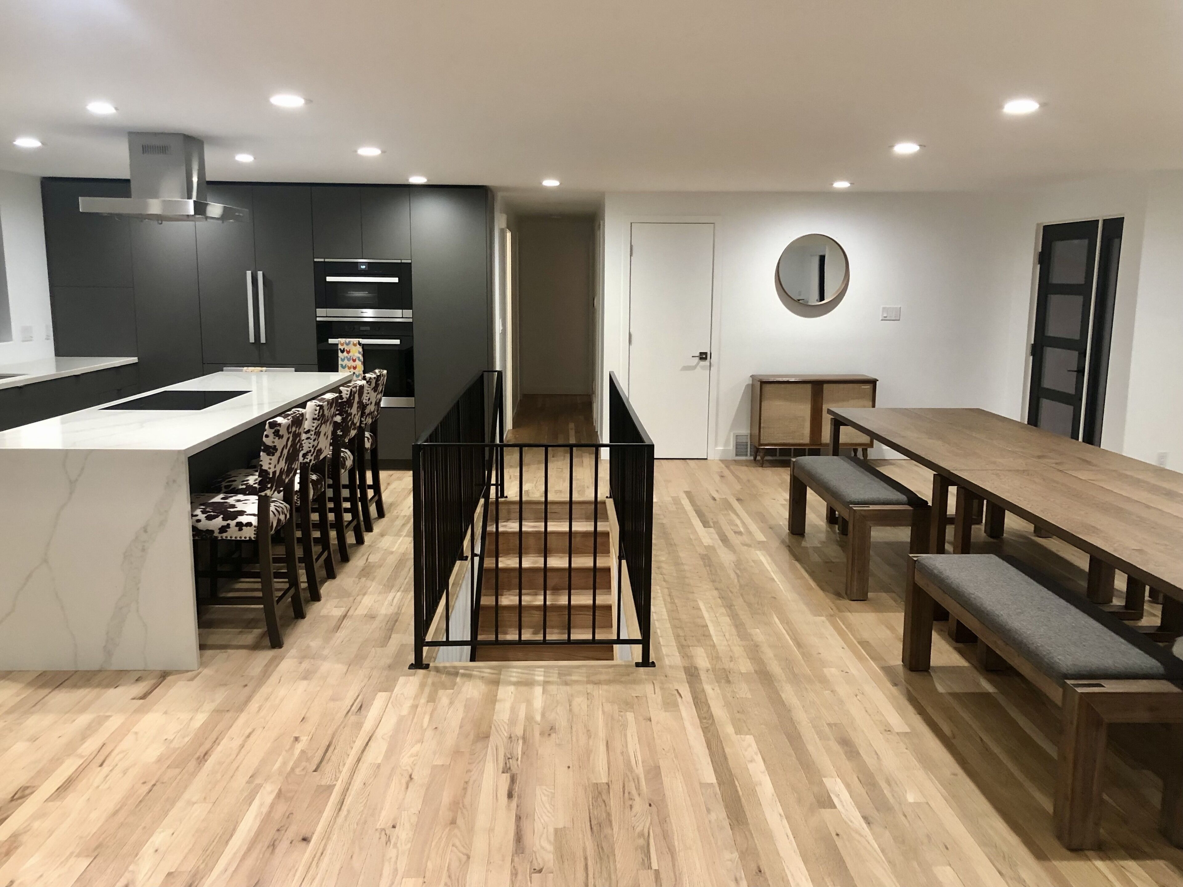Une cuisine moderne dotée d’un îlot central, de meubles de rangement aux couleurs sombres et d’un coin repas avec une table et des bancs en bois.