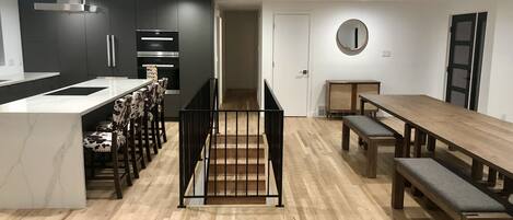 Une cuisine moderne dotée d’un îlot central, de meubles de rangement aux couleurs sombres et d’un coin repas avec une table et des bancs en bois.