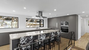 Una cucina moderna con isola centrale, sgabelli da bar, cappa aspirante in acciaio inossidabile e una grande finestra vista innevata.