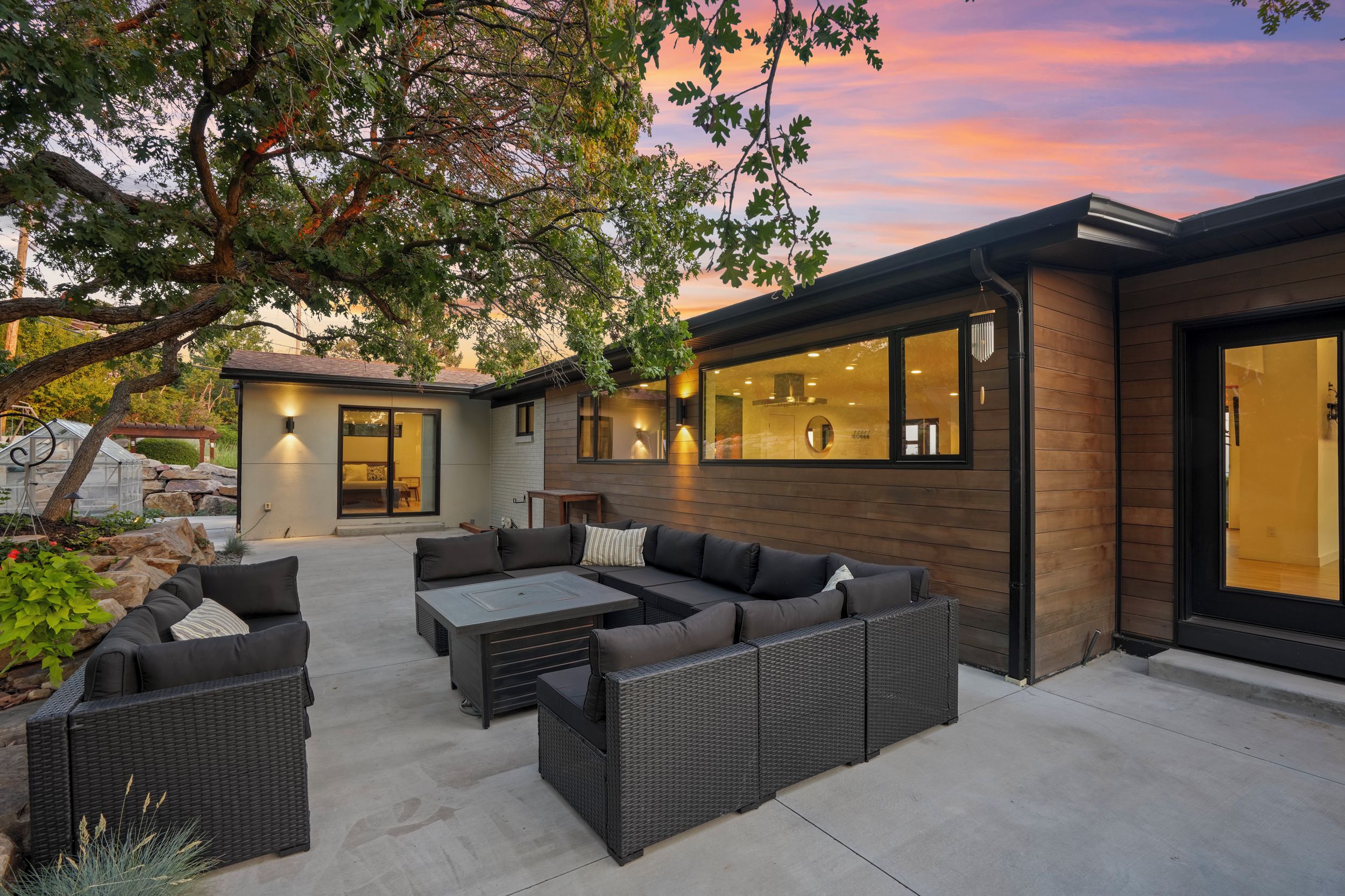 Une maison moderne dotée d’un patio aménagé avec du mobilier d’extérieur et une serre.