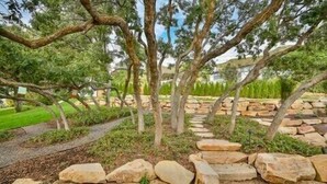 Un giardino curato con un viale in pietra, alberi e un muro di pietra.