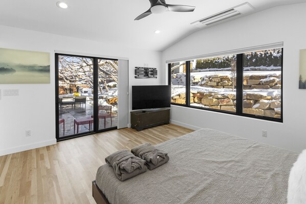 Une chambre moderne dotée d’un grand lit, d’un téléviseur à écran plat et d’une porte-fenêtre coulissante donnant sur un espace extérieur avec vue sur des rochers et des arbres recouverts de neige.