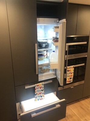Una cocina moderna con refrigerador y horno integrados, que presenta una variedad de alimentos y recipientes.