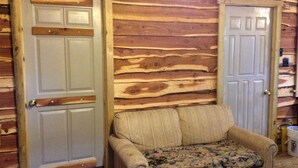 A room with two doors, a patterned sofa, and a wooden wall. - Hickory Hill Cabin Rentals (Clinton)