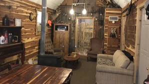 A rustic cabin interior with a wooden interior, a fireplace, a sofa, and a dining table. - Hickory Hill Cabin Rentals (Clinton)