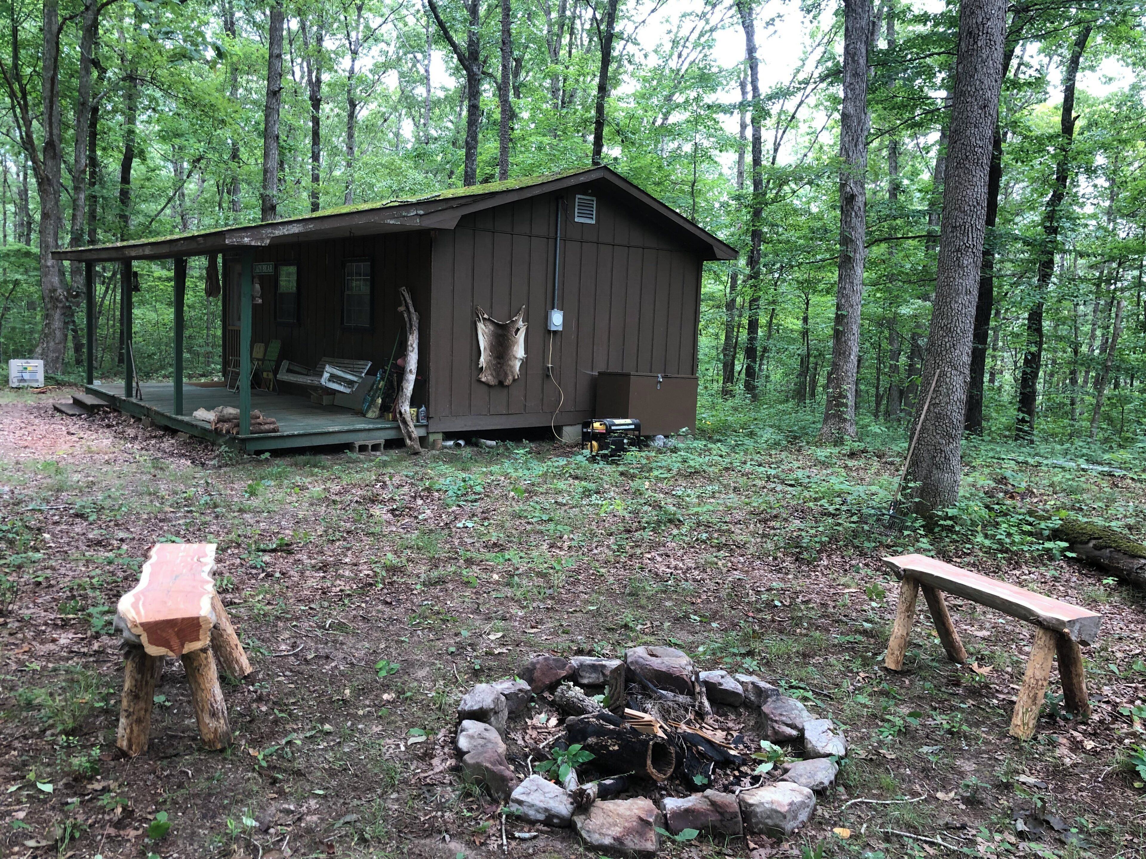 A rustic cabin with a porch, a fire pit, and a bench.