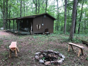 A rustic cabin with a porch, a fire pit, and a bench.