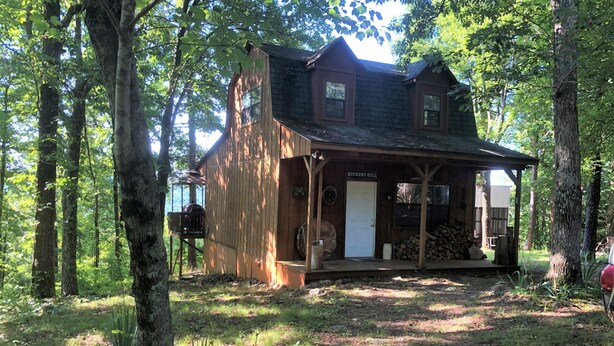 A rustic cabin with a porch, surrounded by trees. - Hickory Hill Cabin Rentals (Clinton)