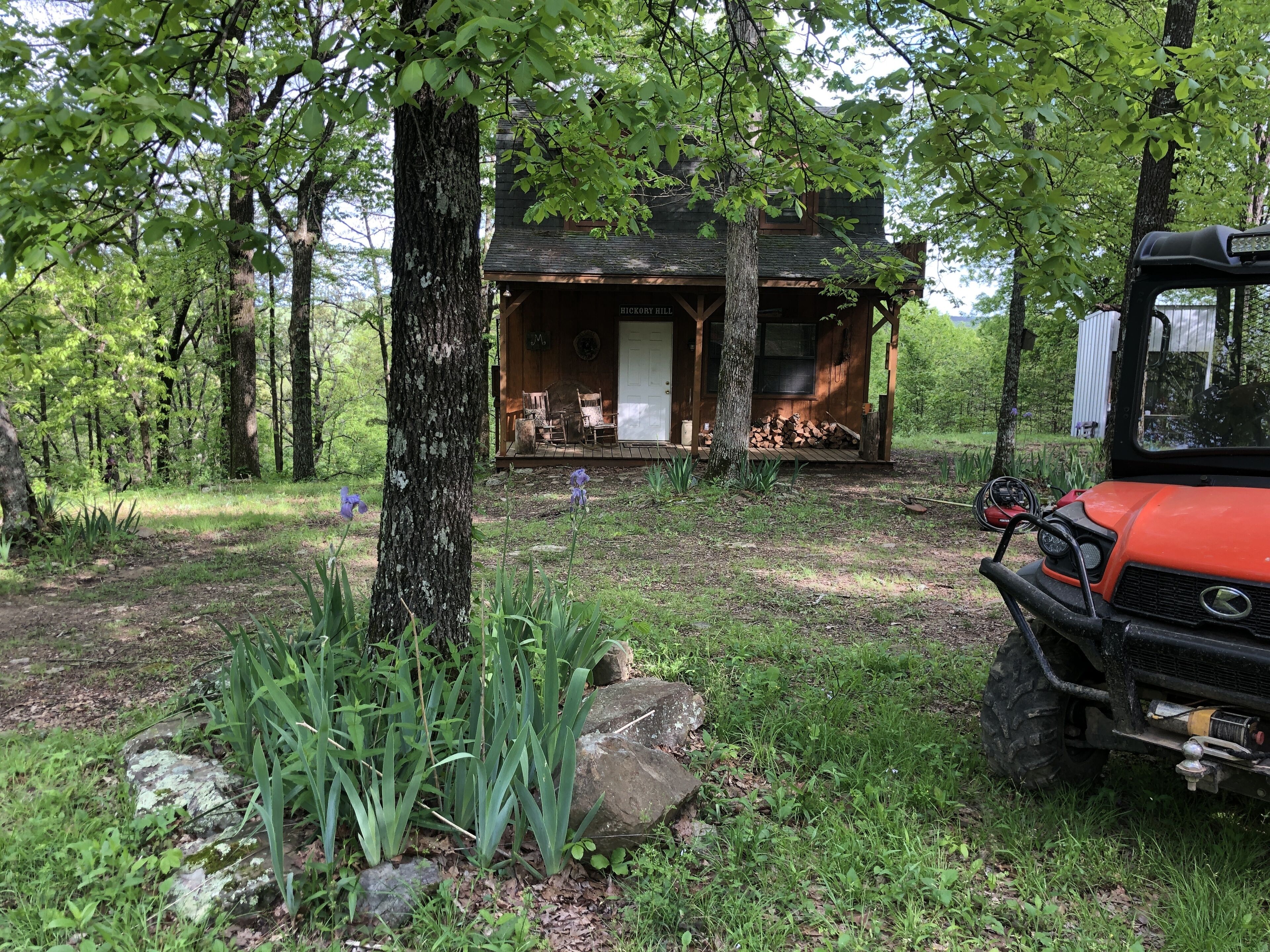 A cabin with a porch, surrounded by trees and a lawn.