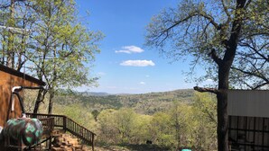 A rustic cabin with a staircase leading to a deck, surrounded by trees and a view of distant hills. - Hickory Hill Cabin Rentals (Clinton)