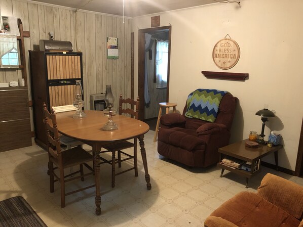 Uma sala de estar aconchegante com uma mesa de jantar de madeira, uma poltrona confortável e uma pequena mesa lateral com abajur.