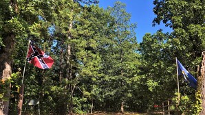 A forested area with a dirt path, a Confederate flag, and a blue flag. - Hickory Hill Cabin Rentals (Clinton)
