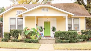A two-story house with a front porch, a green door, and a small garden with potted plants. - J Birds' Bungalow (Memphis)