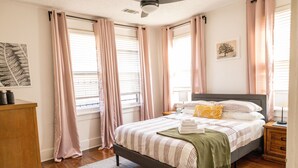 A bedroom with a bed, bedside tables, a nightstand, a ceiling fan, and a window with curtains. - J Birds' Bungalow (Memphis)