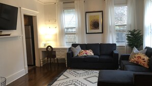 A living room with a dark sofa, a patterned rug, a small side table, and a television on a stand. - J Birds' Bungalow (Memphis)