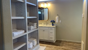 A bathroom with a vanity, a mirror, a towel rack, and a shelf with folded towels. - Taylor II House, ocean view, close to everything (Crescent City)