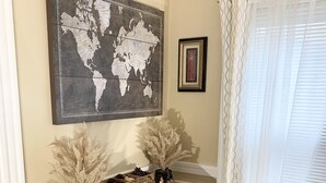 Uma sala de jantar com uma mesa de madeira, armários brancos, uma obra de arte com um mapa-múndi e uma janela com cortinas brancas.