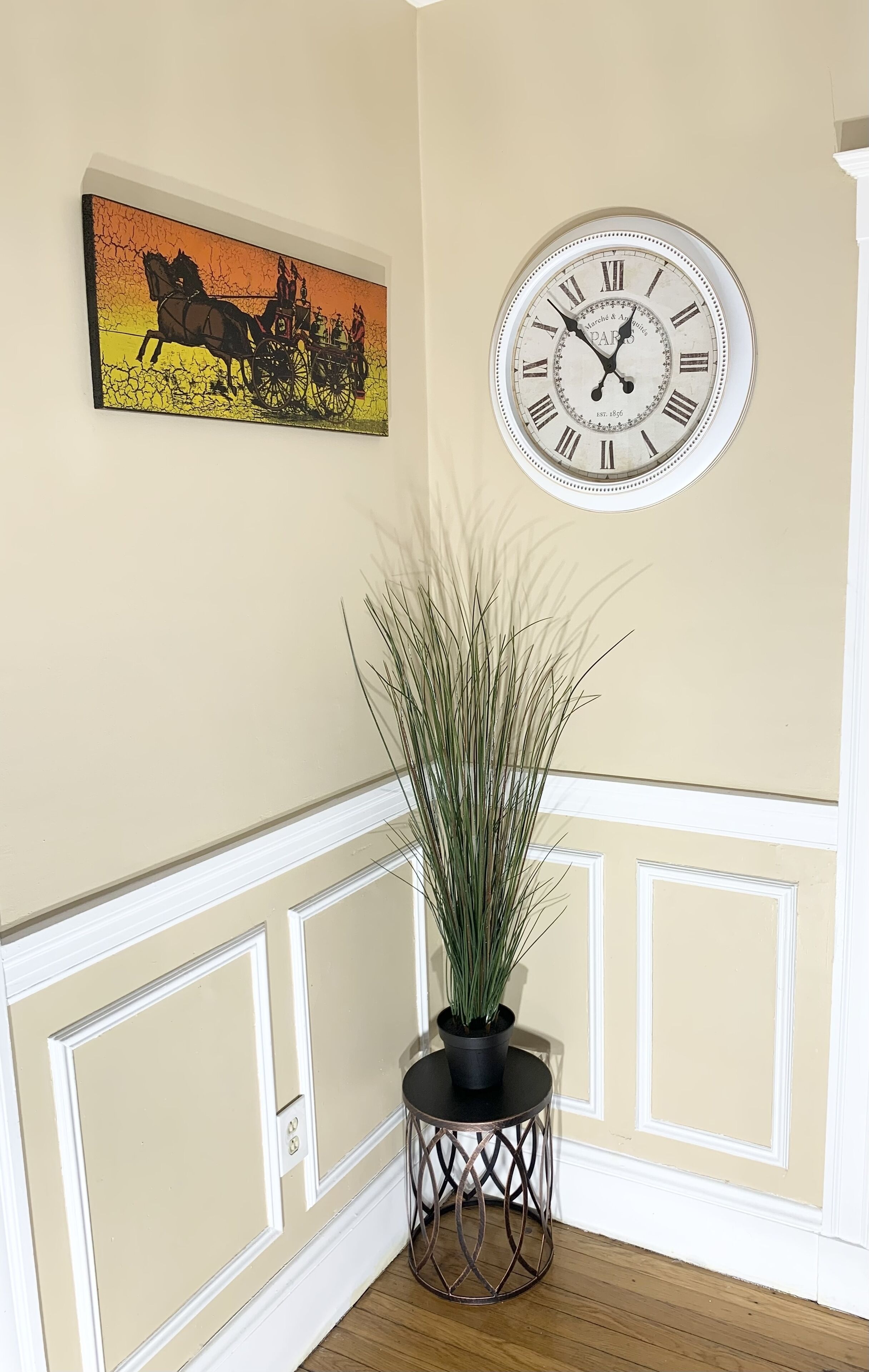 Una habitación con un reloj en la pared, un cuadro enmarcado y una planta en maceta.