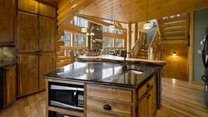 A spacious kitchen with wooden cabinets, a large island, and a stone fireplace. - Custom Log Cabin Close to Cades Cove in GSMNP! (Townsend)