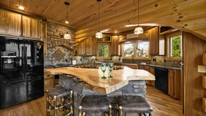 A spacious kitchen with a large island, wooden cabinets, and a stone backsplash. - Custom Log Cabin Close to Cades Cove in GSMNP! (Townsend)