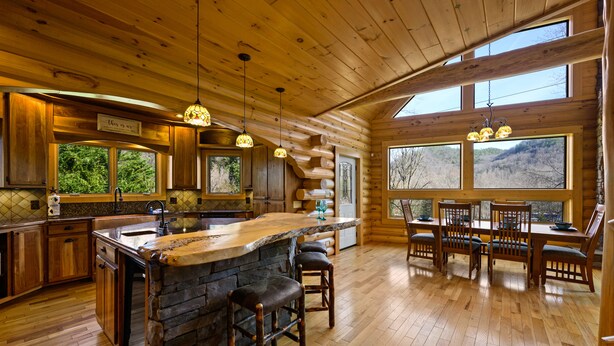 A log cabin with a kitchen featuring a stone island, wooden bar stools, and a dining area with a table and chairs. - Custom Log Cabin Close to Cades Cove in GSMNP! (Townsend)
