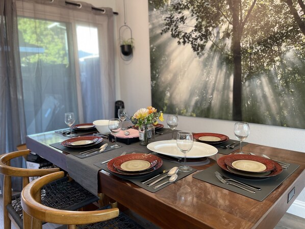 Una mesa de comedor preparada con platos, vasos y cubiertos, con vistas a los árboles a través de la ventana.