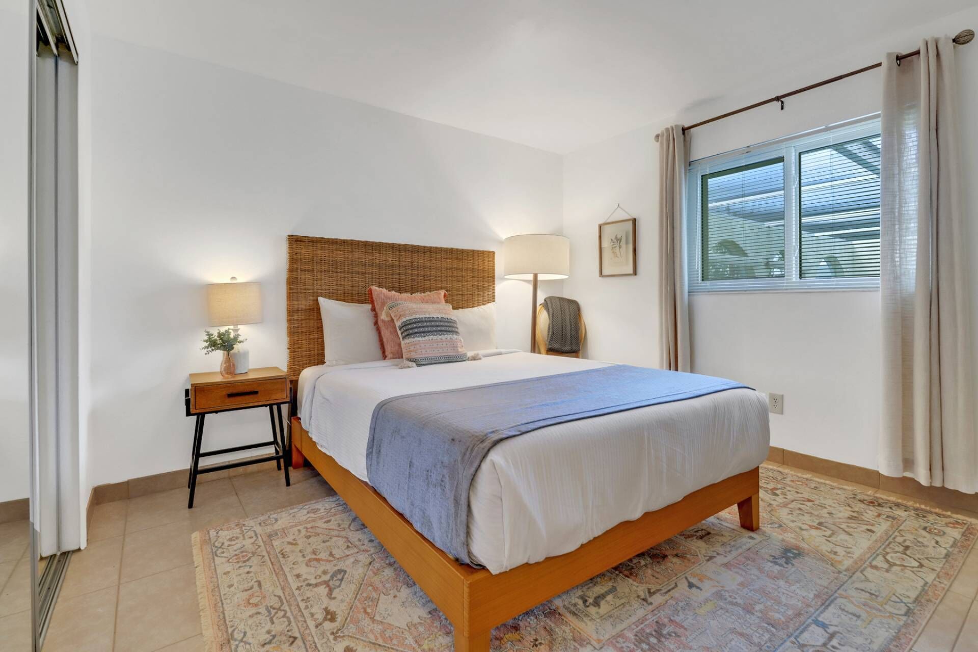 A bedroom with a wooden bed, a nightstand, a lamp, and a window with curtains.