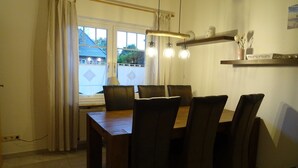 Un comedor con una mesa de madera y seis sillas, una ventana con cortinas y una lámpara colgante.