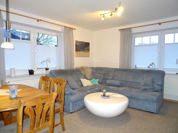 A living room with a grey sofa, wooden chairs, a round coffee table, and a painting on the wall.