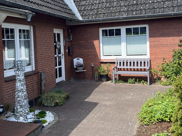 A brick house with a white door, a white bench, and a potted plant. - Nord-Ostsee-Nest: Apartment with sun terrace and wallbox - Nord-Ostsee-Nest (Tarp)