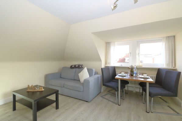 Un salon avec un canapé gris, une petite table et un coin repas comprenant des chaises et une table.