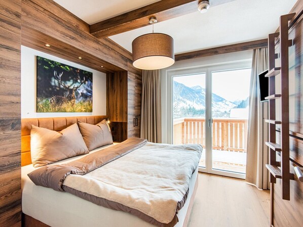 Quarto com cama grande, paredes de madeira, TV na parede e varanda com vista para as montanhas.