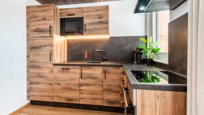 Une cuisine moderne avec des armoires en bois, un four à micro-ondes encastré, un évier en acier inoxydable et une hotte de cuisine noire.