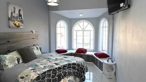 Une chambre à coucher avec un lit, un coin fenêtre et un téléviseur fixé au mur.