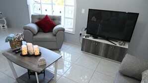 Un salon moderne avec un canap é gris, un coussin rouge, un téléviseur posé sur un meuble en bois et une table avec des bougies.