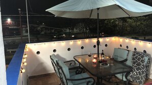 Un espace extérieur aménagé avec une table et des chaises, des guirlandes lumineuses et un parasol blanc.