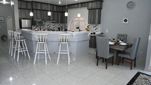 Une cuisine moderne dotée d’un îlot central, de tabourets de bar, d’une table à manger avec des chaises et de luminaires suspendus.