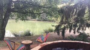 Een hottub met twee kleurrijke stoelen op een houten terras, met uitzicht op een kalm vijver.