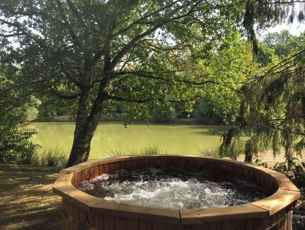A wooden hot tub surrounded by trees and a body of water.